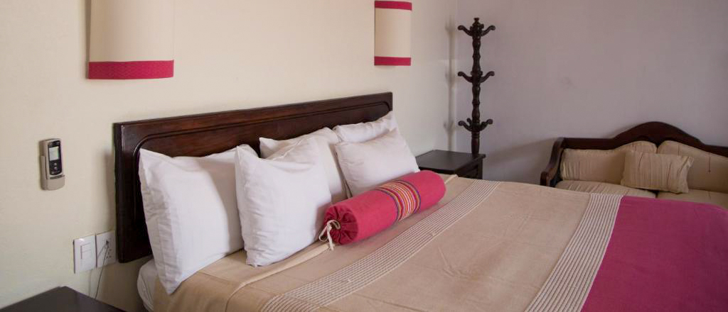A comfortable hotel room in Oaxaca with a large bed, white pillows, and a pink throw.