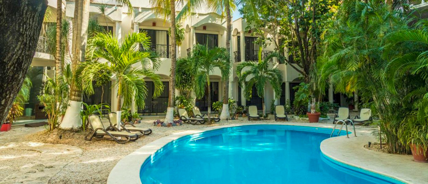 Relaxing hotel pool area in Playa del Carmen with lounge chairs and lush tropical plants.