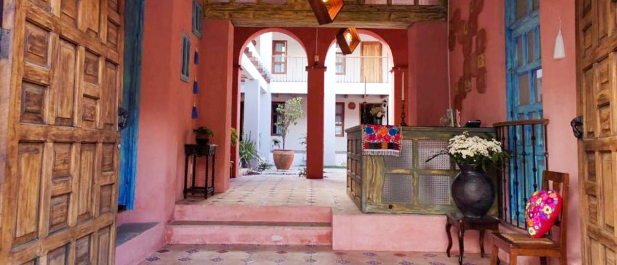 A charming hotel courtyard in San Cristobal de las Casas with bright pink walls and wooden doors.