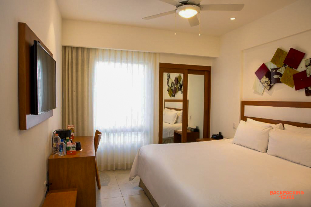 A bright and comfortable hotel room in Cancun with a large bed, desk, and window.
