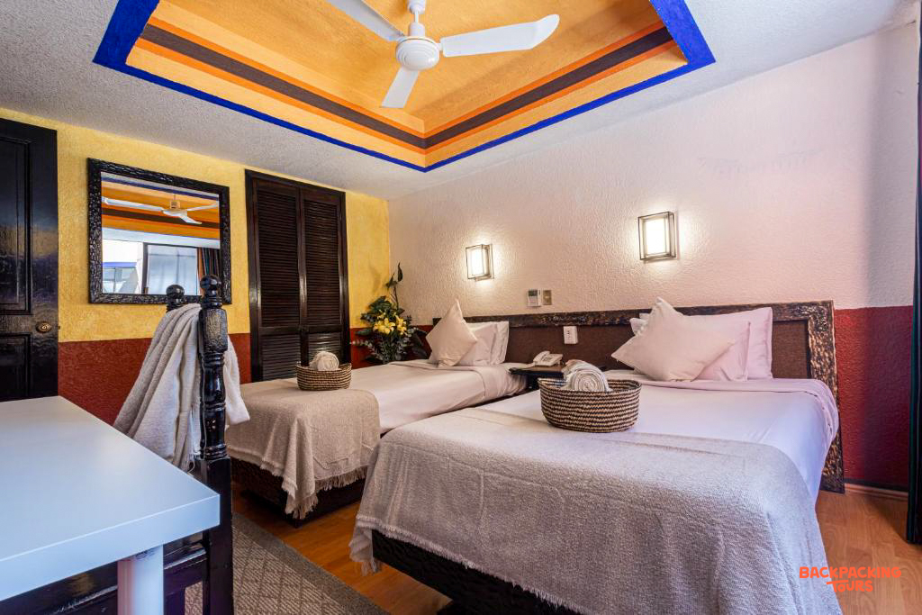 A vibrant hotel room in Mexico City with two comfortable beds, a colorful ceiling, and warm lighting.