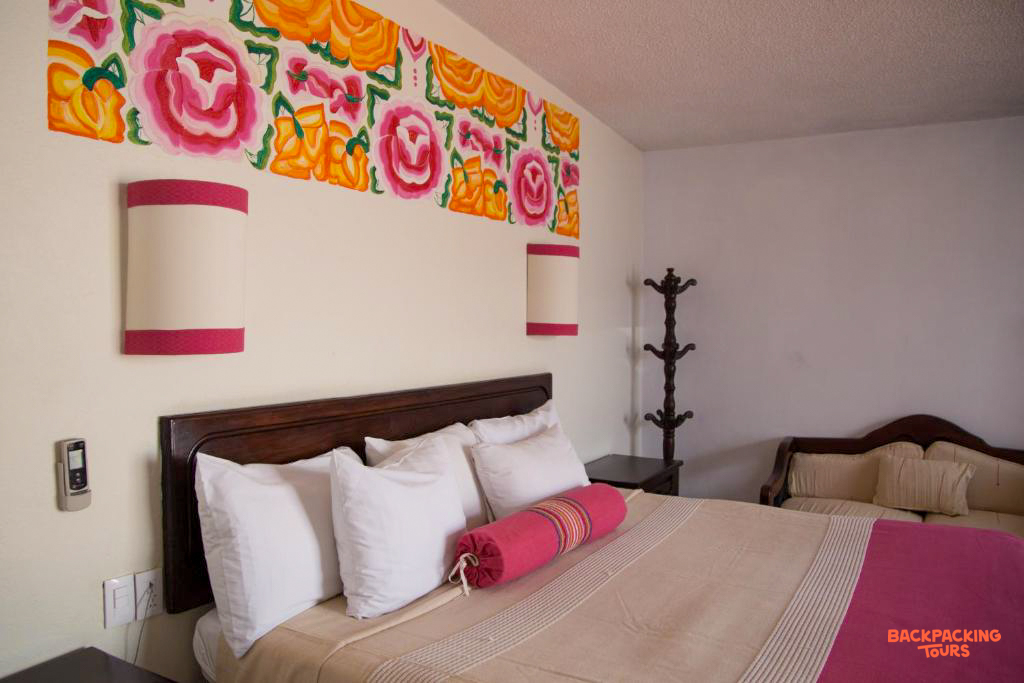 A comfortable hotel room in Oaxaca featuring a vibrant floral mural above the bed and cozy furnishings.