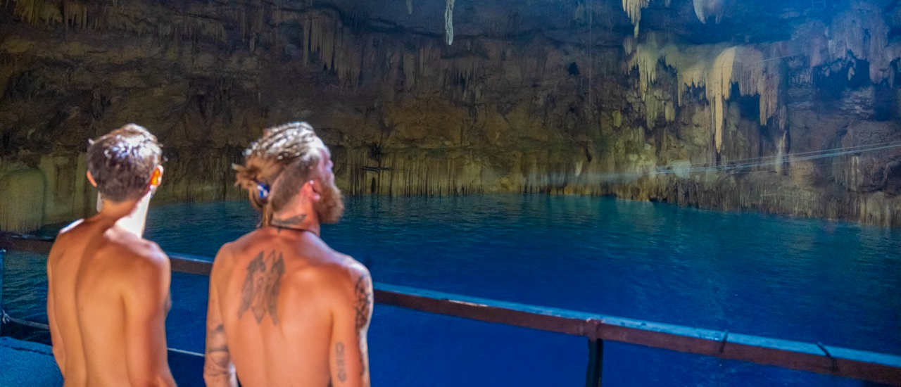 Two men look out at the clear blue water of an underground cenote in Mexico.