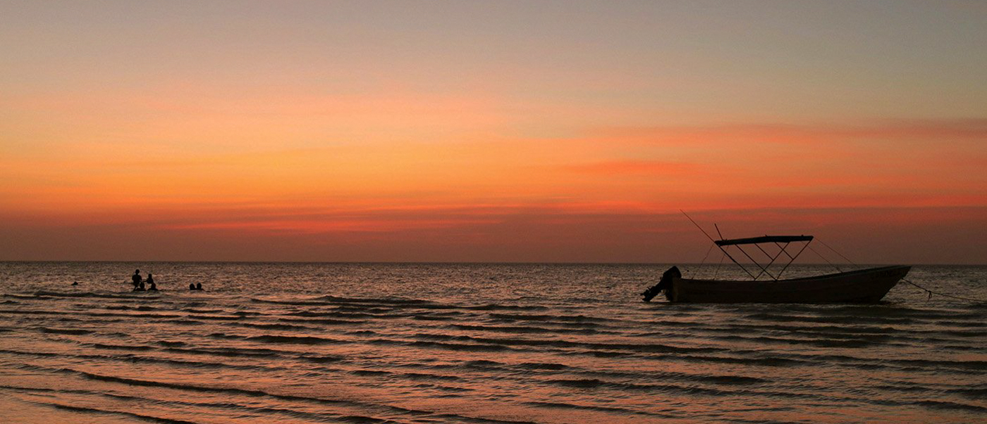 Silhouetted boat and people enjoying a vibrant orange sunset over the calm waters of Playa del Carmen.