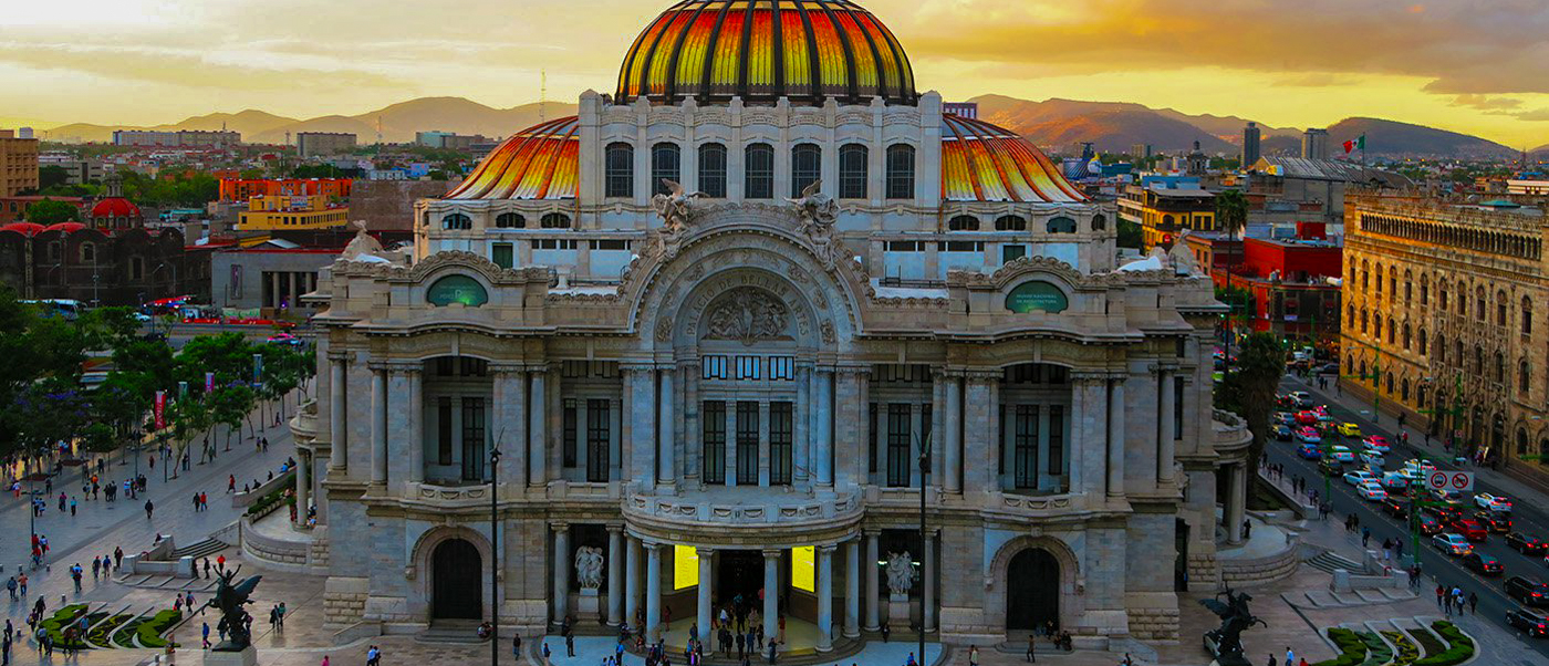 The grand Palacio de Bellas Artes in Mexico City at sunset, with people walking in the plaza.