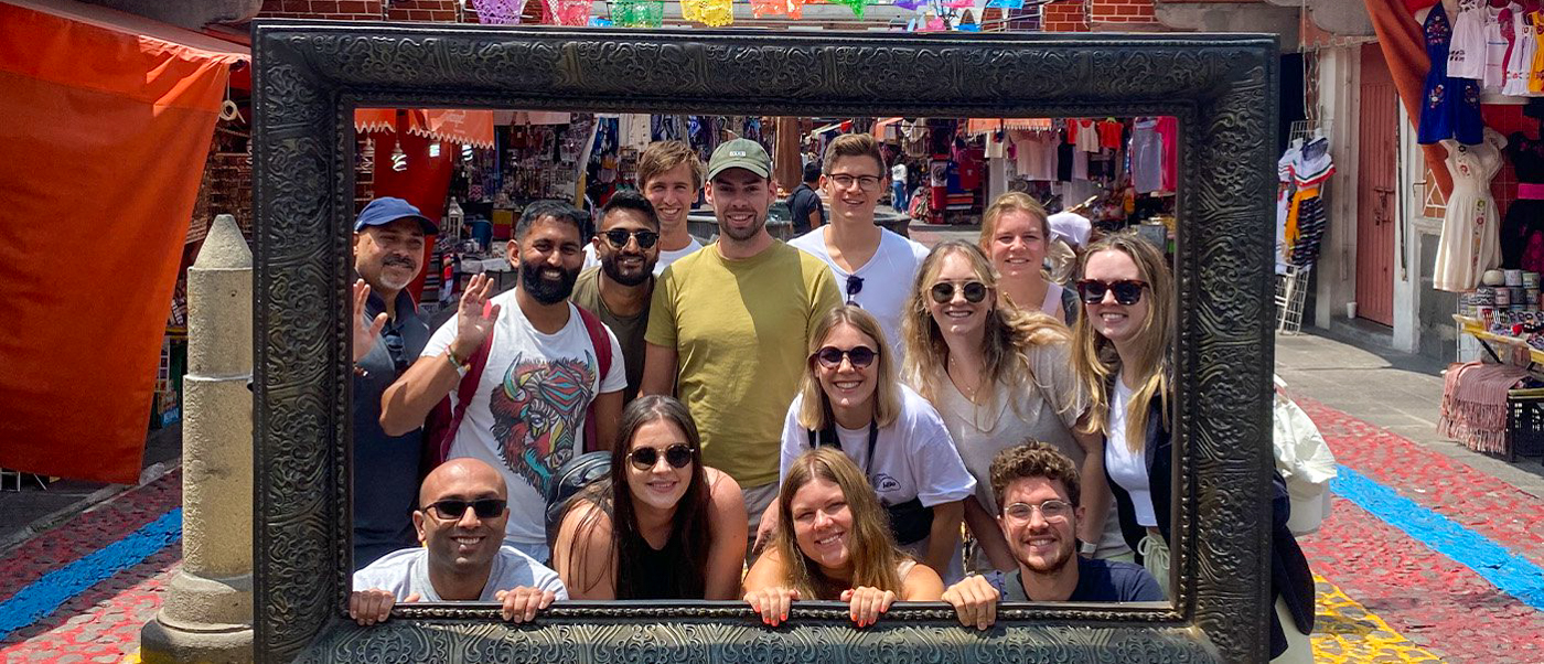 A happy group of travelers poses in a large frame on a colorful, buzzing street in Oaxaca.