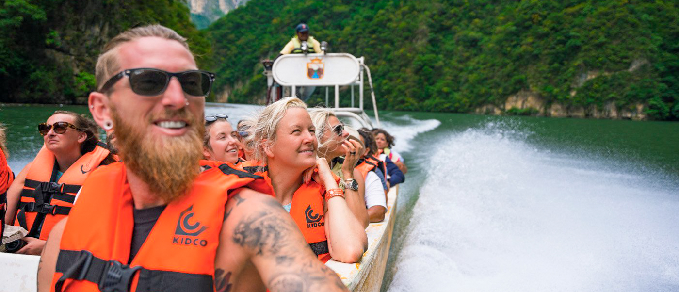 Smiling tourists in life vests enjoying a fast boat ride through the lush Sumidero Canyon.