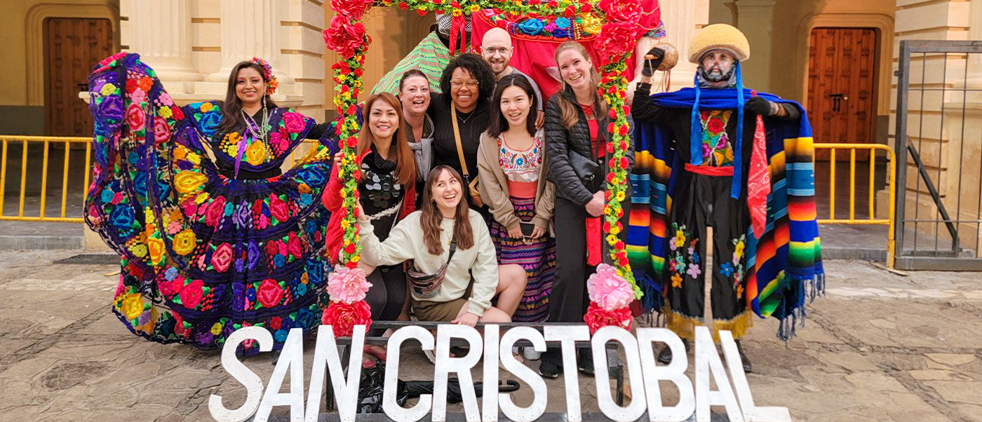 Happy tourists pose with a woman in traditional dress and a cultural figure in San Cristobal, Mexico.