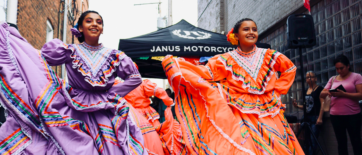 Two smiling women in vibrant traditional Mexican dresses joyfully dancing at an outdoor festival in San Cristobal.