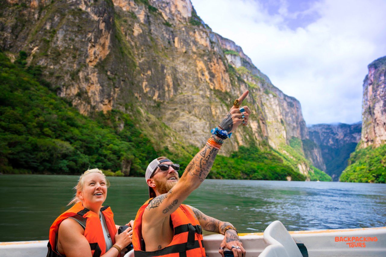 Happy travelers on a boat cruise through Sumidero Canyon, pointing up at the majestic towering cliffs.