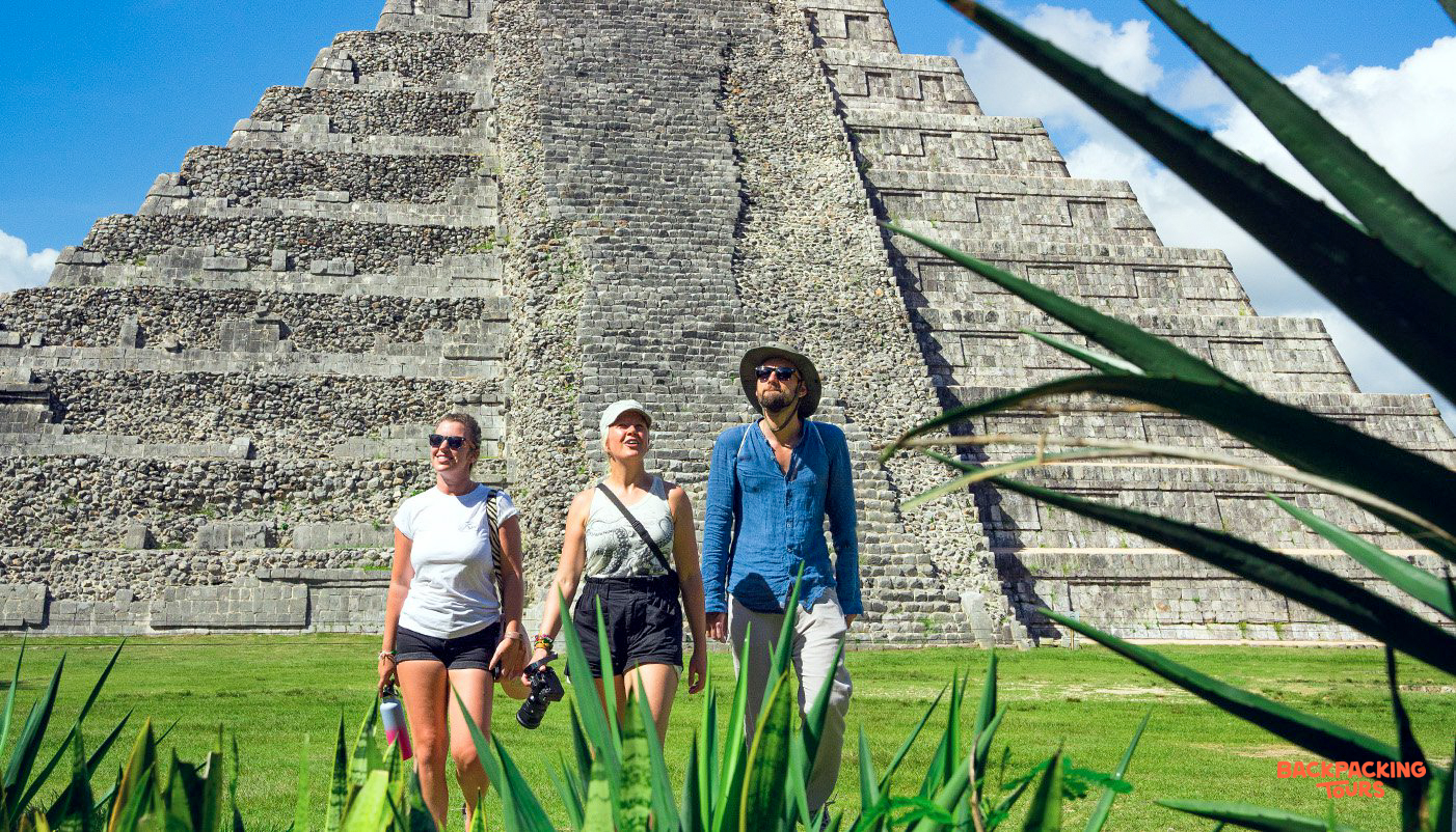 Three travelers admire the ancient Mayan pyramid of Chichén Itzá on a sunny day.
