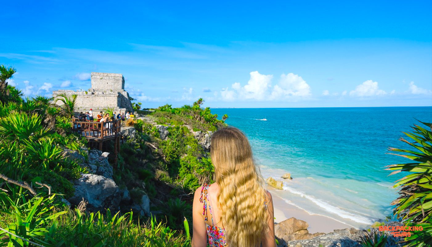 A person views the ancient Tulum Ruins overlooking a stunning Caribbean beach.