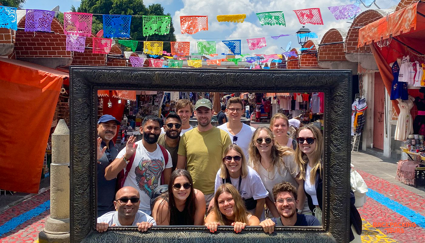 Smiling friends pose in a large decorative frame under colorful papel picado banners in Oaxaca.