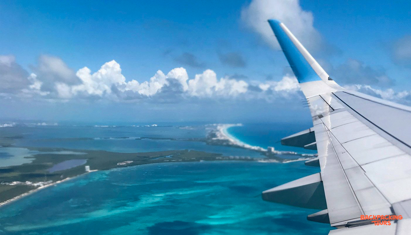 An airplane wing overlooks the stunning turquoise Caribbean waters and white beaches of Cancun.