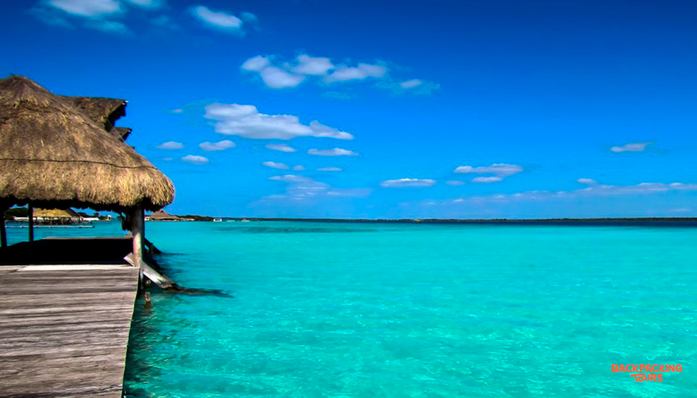 A thatched-roof palapa over clear turquoise waters under a bright blue sky on Isla Holbox.