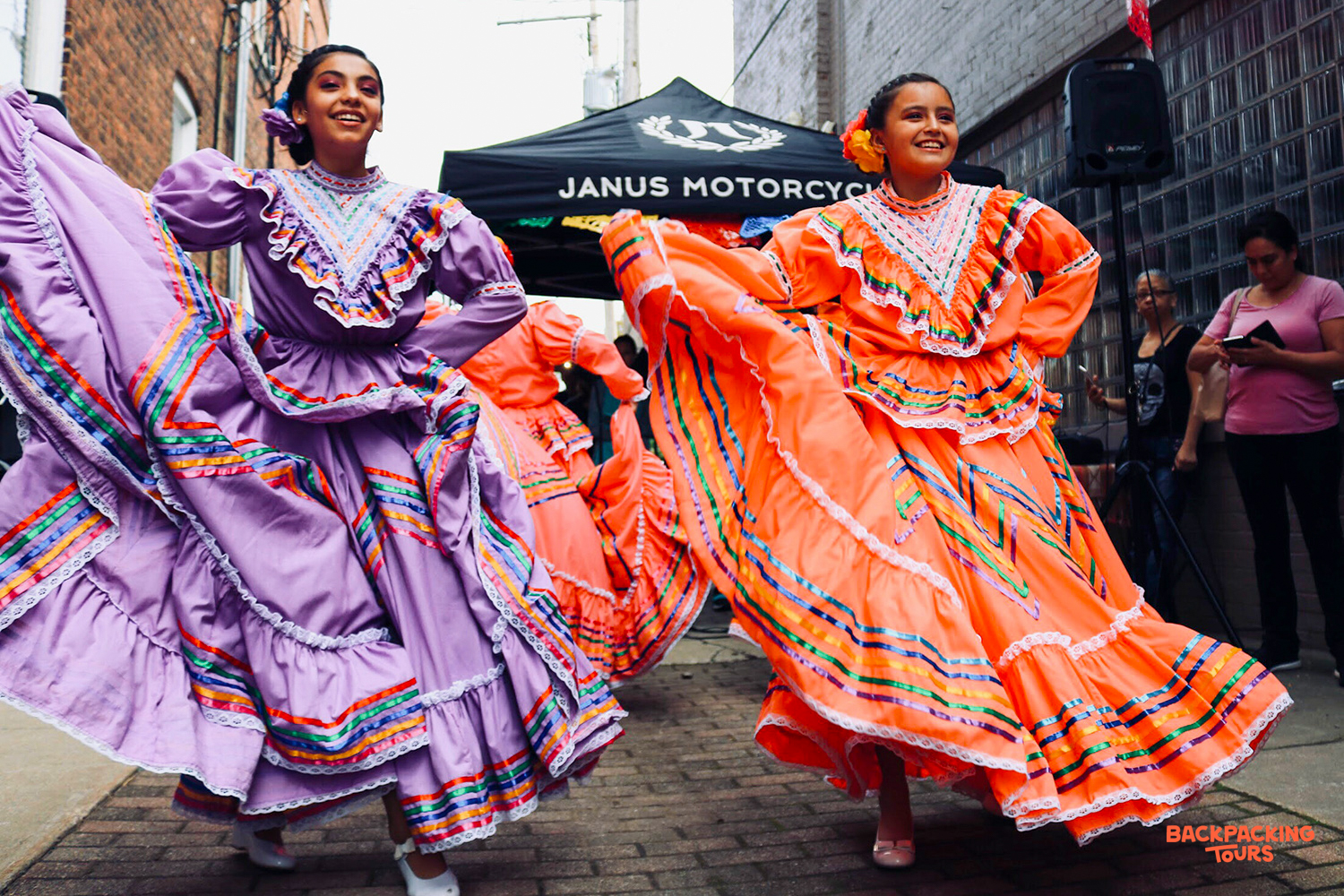 Two smiling young women in vibrant traditional Mexican dresses dance joyfully in San Cristobal.