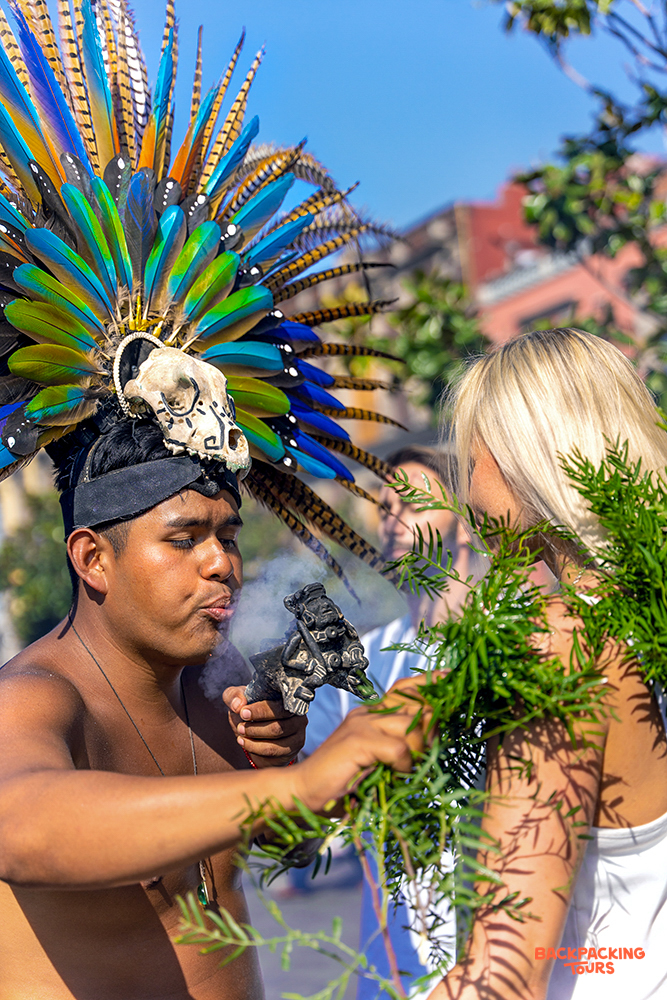 A local man in Mexico performs a traditional smoke blessing on a blonde traveler.