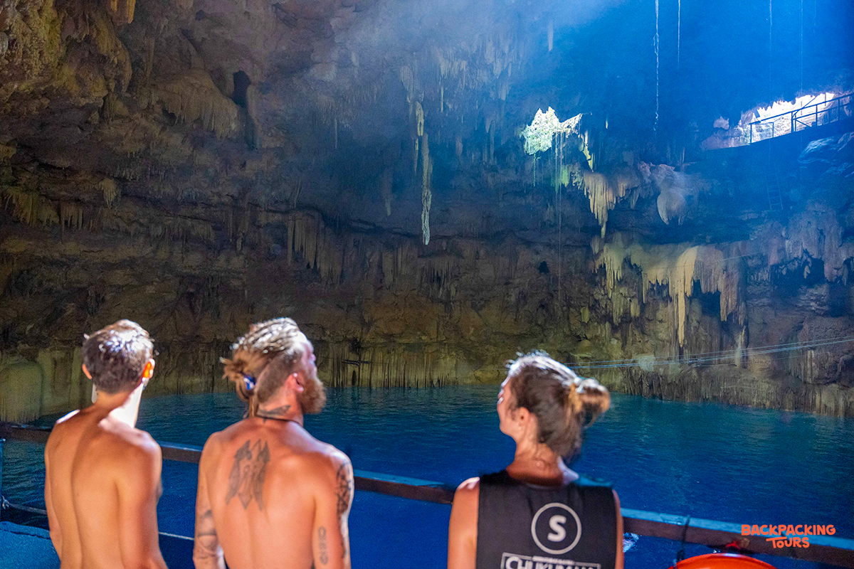 Three friends look up at the beautiful light filtering into an underground cenote in Mexico.