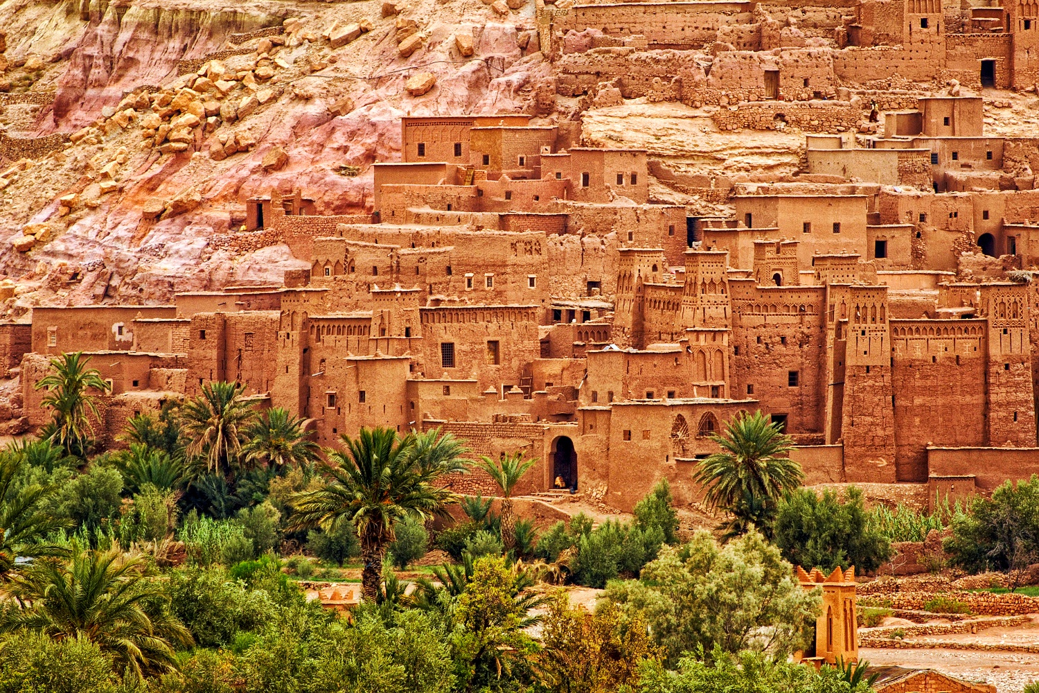 Historic fortified village of Ait Benhaddou, Morocco, nestled against a dry mountain with a green oasis.