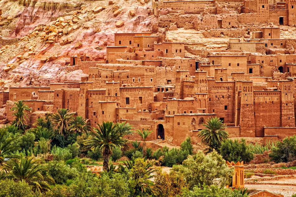 Historic fortified village of Ait Benhaddou, Morocco, nestled against a dry mountain with a green oasis.