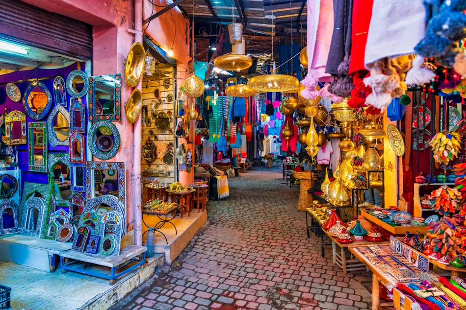 A vibrant Moroccan market alley filled with colorful lamps, handcrafted mirrors, and textiles.