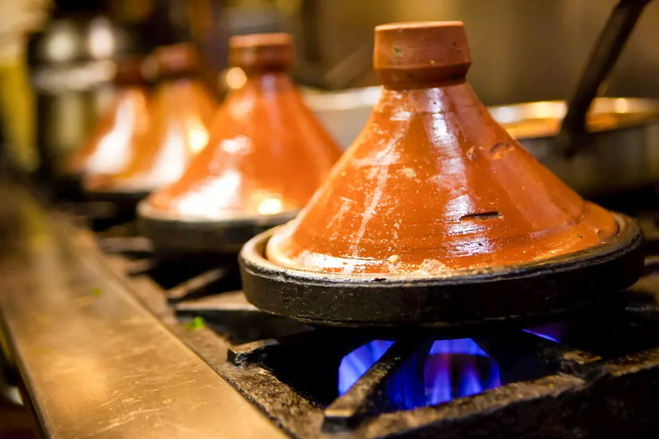 Authentic Moroccan tagines simmering over blue flames on a kitchen stove.