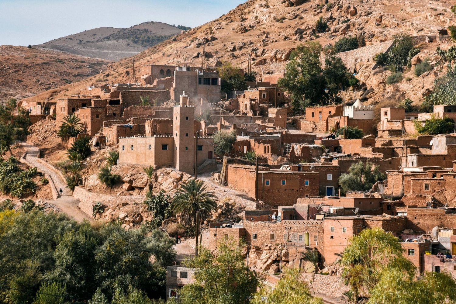 Traditional mud-brick village nestled among green trees in the arid High Atlas Mountains of Morocco.