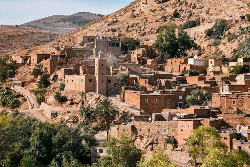Traditional mud-brick village nestled among green trees in the arid High Atlas Mountains of Morocco.