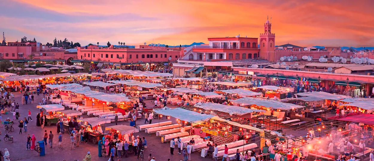 A bustling market square in Marrakech filled with people and illuminated stalls at a vibrant sunset.