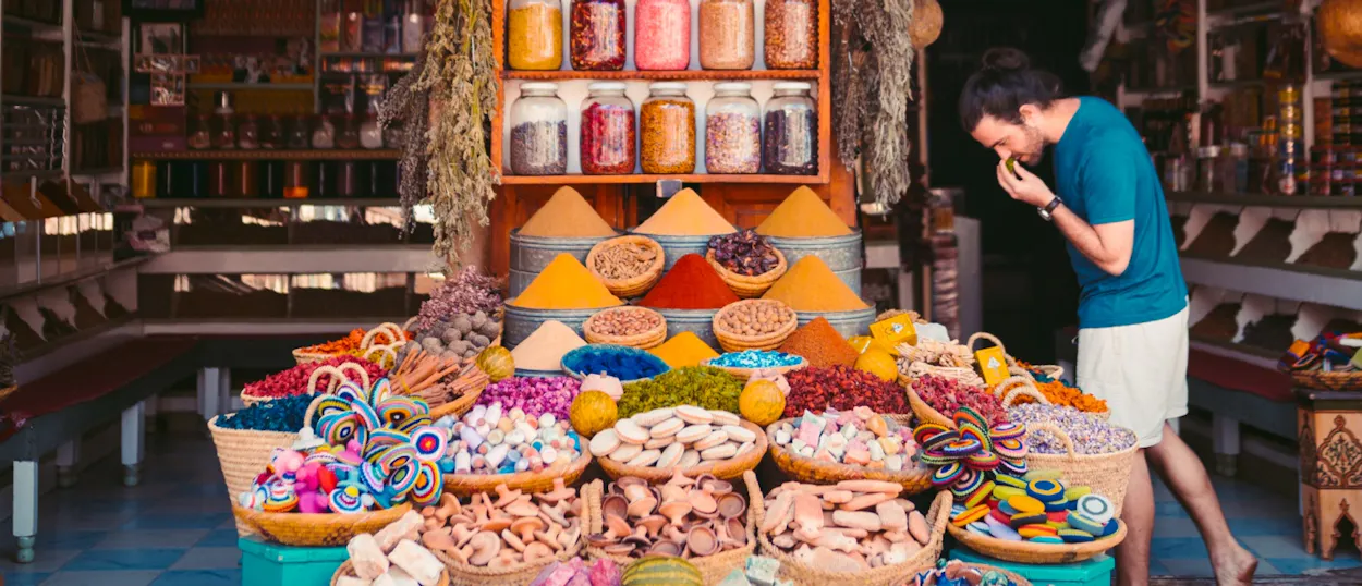 A man enjoying the fragrant aroma of colorful spices displayed in a bustling Marrakech souk.