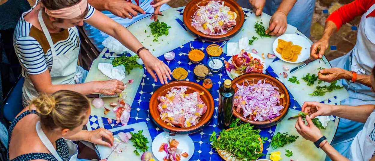 Tourists actively chop fresh vegetables and herbs during a lively Moroccan cooking class in Imlil.