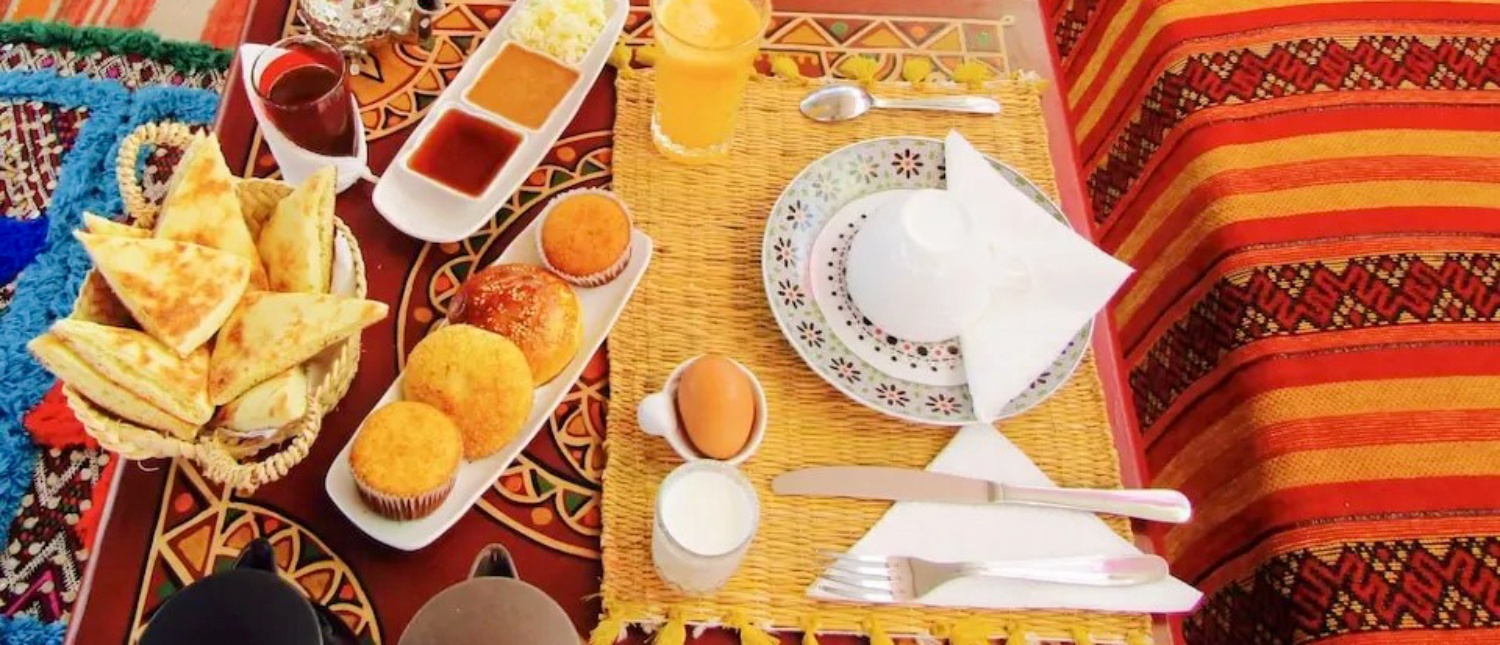 A colorful Moroccan breakfast featuring pastries, juice, and spreads on intricately patterned textiles in Marrakech.