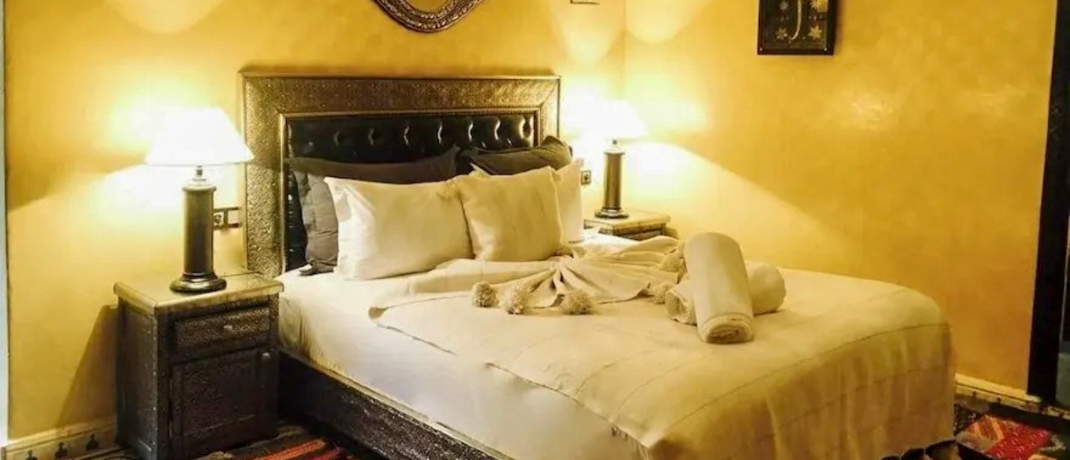 A warm and inviting bedroom in a Marrakech riad with a large bed and ornate headboard.