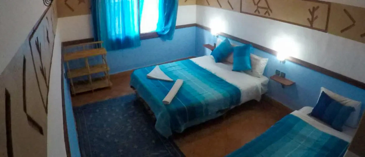 A cozy hotel room in Dades Valley with two beds, blue bedding, and patterned walls.