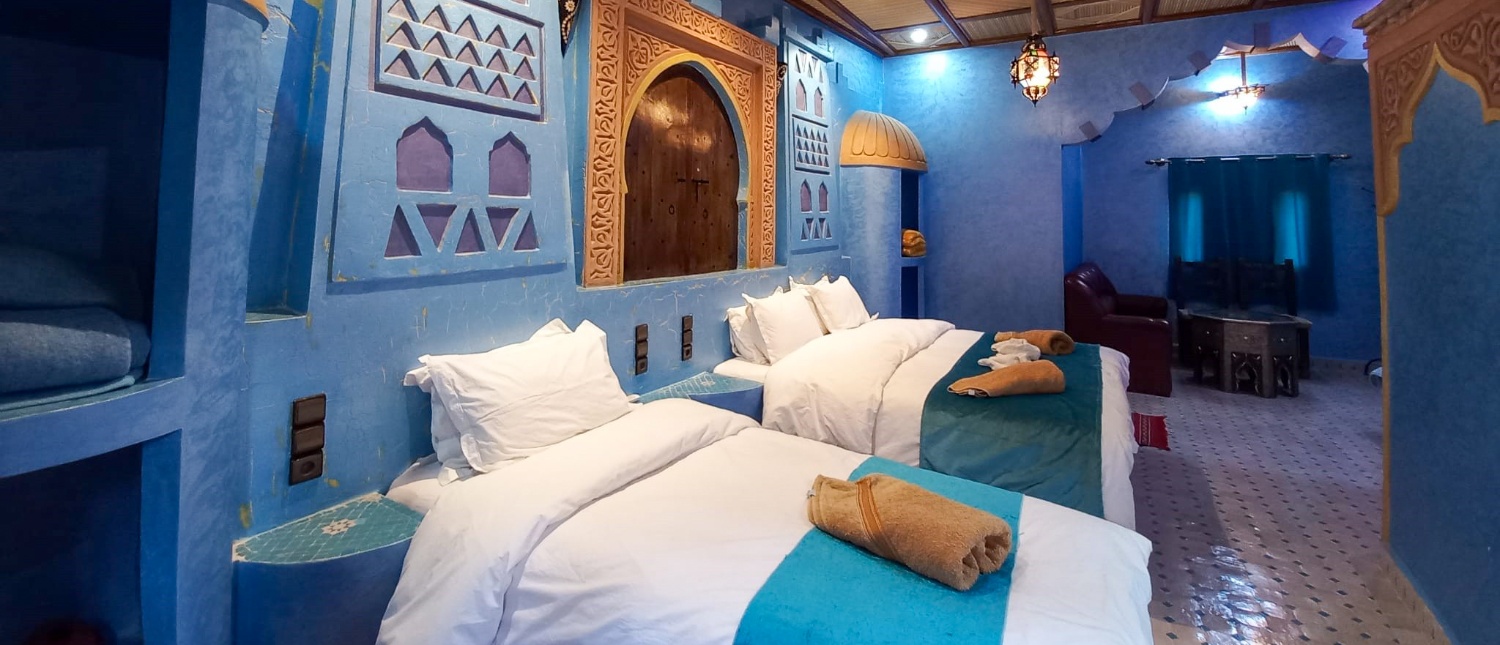 A vibrant blue Moroccan hotel room with three beds and traditional decor, offering a cozy stay.