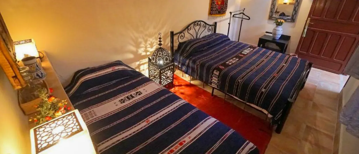 A welcoming hotel room in Ouarzazate featuring two beds with patterned blankets and decorative lamps.