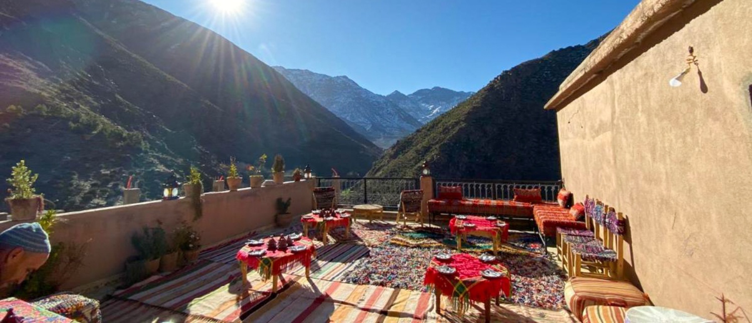Sunny terrace set for breakfast with colorful rugs, overlooking snowy Atlas Mountains in Imlil.