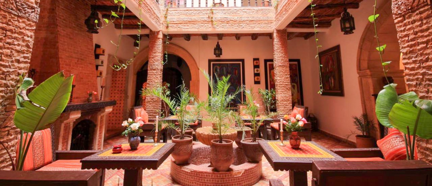 An inviting traditional Moroccan riad courtyard in Essaouira, featuring brick arches, lush plants, and comfortable seating.