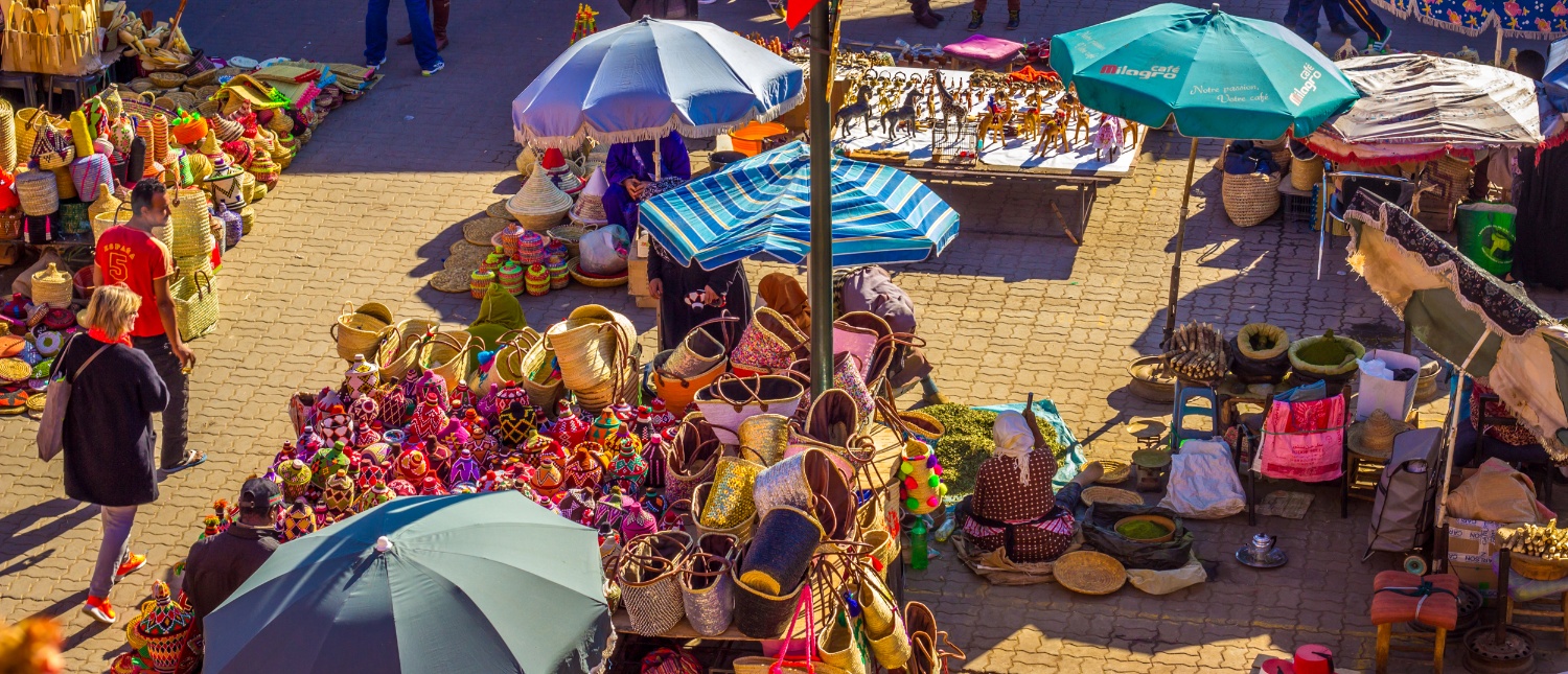 People browse colorful stalls filled with baskets and crafts at a bustling market in Marrakech.