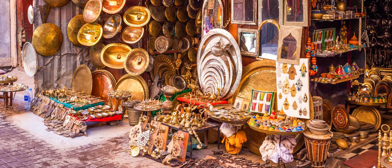 A vibrant market stall in Marrakech showcasing an abundance of traditional brassware, mirrors, and artisan crafts.