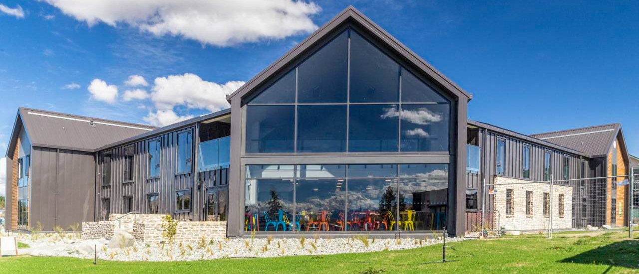 Modern YHA hostel building in Lake Tekapo with large glass windows and colorful chairs inside.