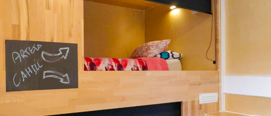 A comfortable wooden bunk bed with colorful bedding and a reading light in a Taupo hostel.