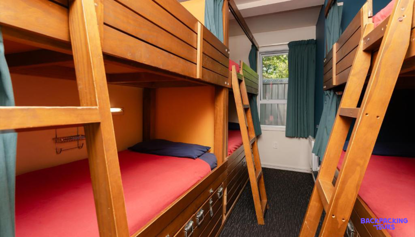 Comfortable wooden bunk beds with red sheets in a hostel dorm room in Queenstown, New Zealand.