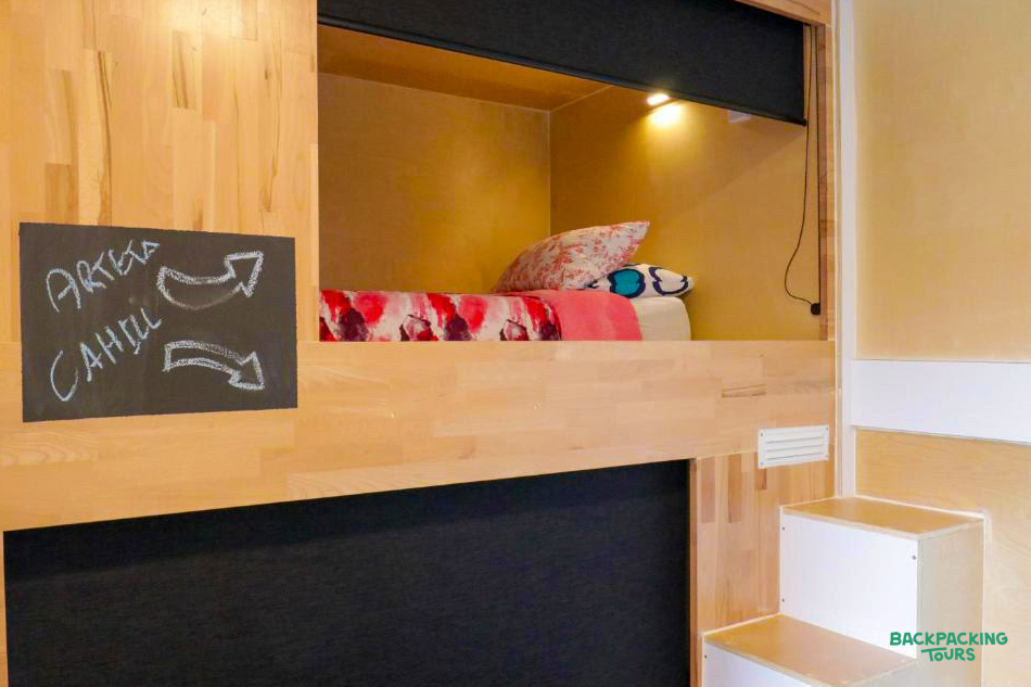 A cozy wooden bunk bed with a reading light and colorful bedding in a Taupo hostel.