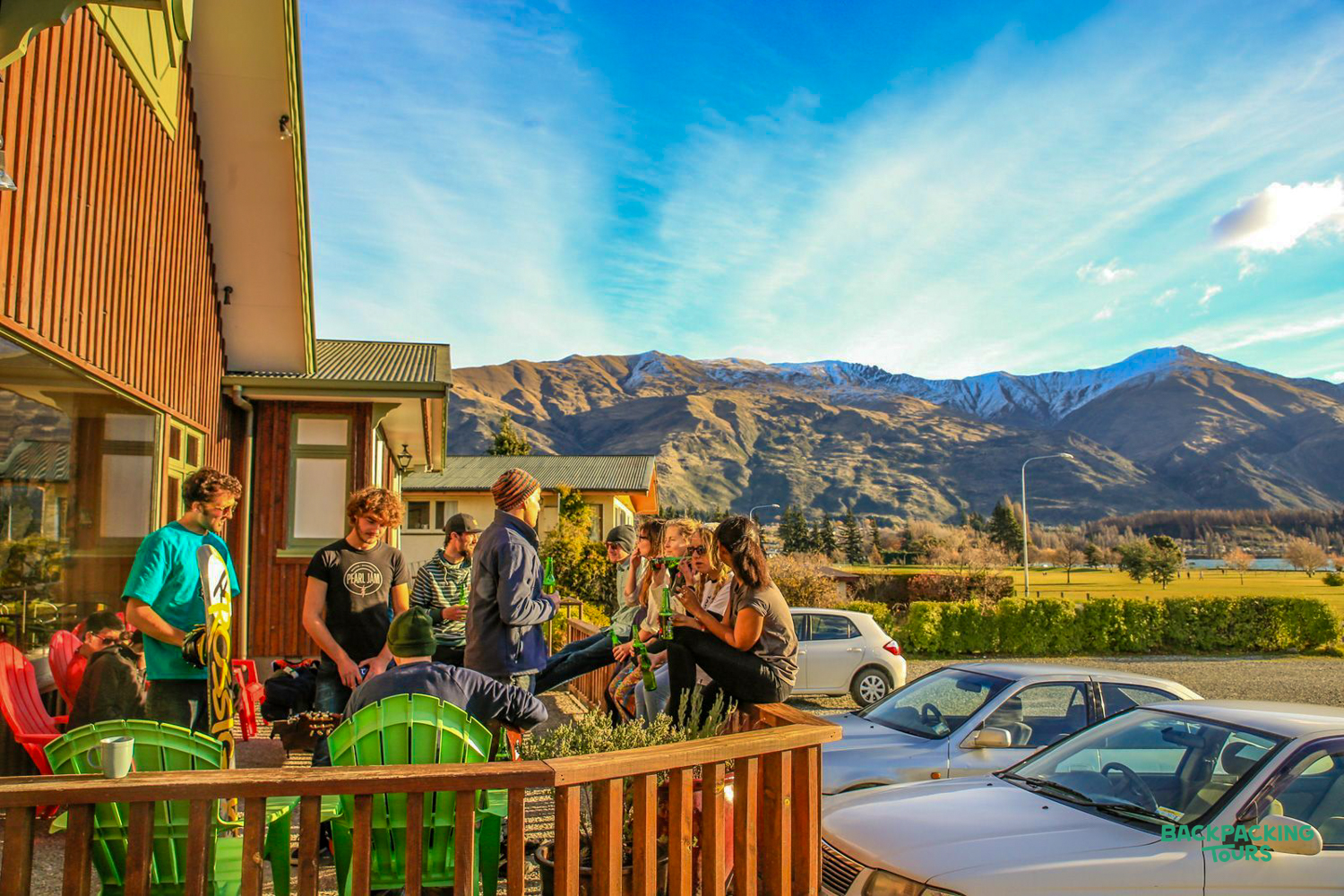 Backpackers relax on a sunny hostel patio in Wānaka, enjoying views of the snow-capped mountains.