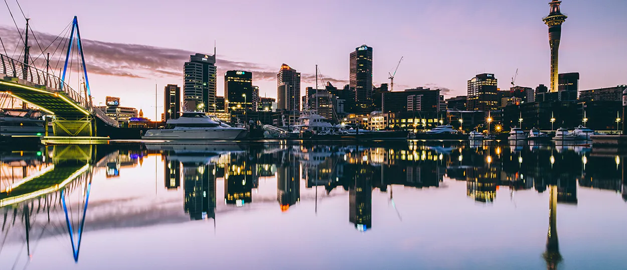 Auckland's vibrant city skyline at twilight, with the Sky Tower and boats reflected in the calm harbor.