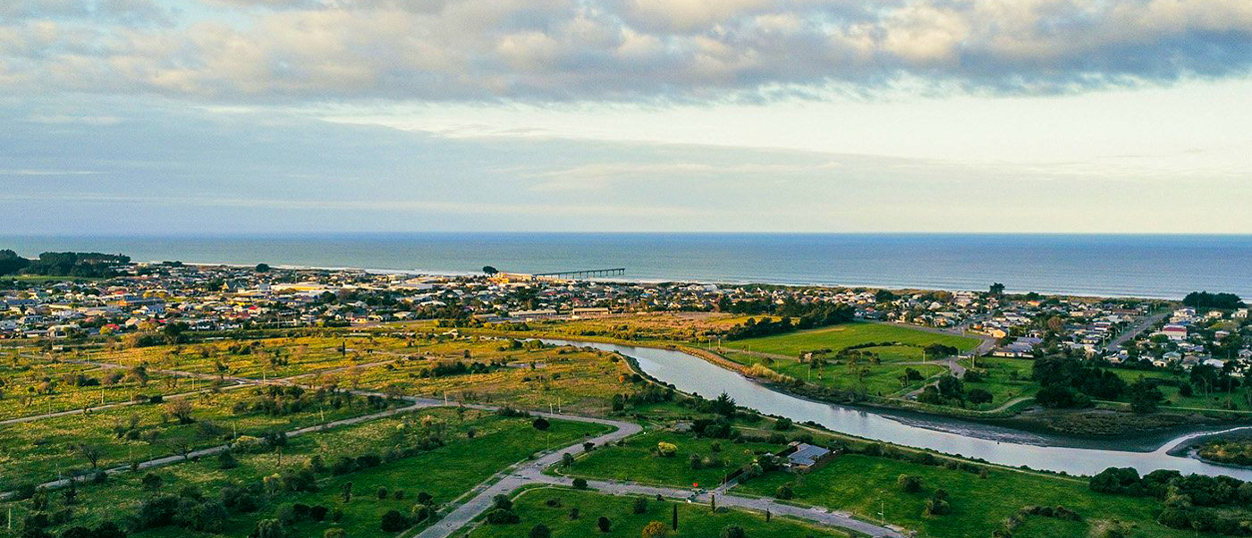Aerial view of Christchurch, a coastal city with a river flowing through green fields to the ocean.