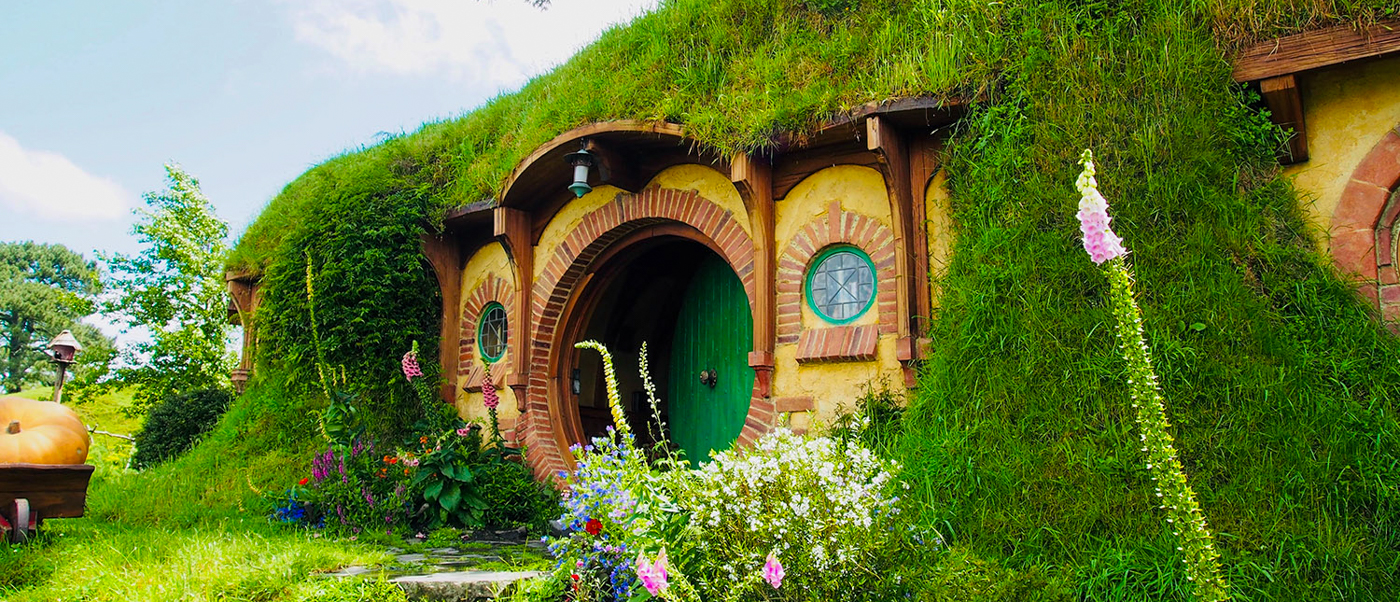 A charming hobbit hole with a round green door nestled into a grassy hill at Hobbiton, New Zealand.
