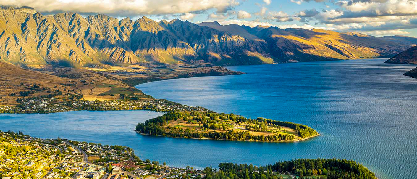 Queenstown, New Zealand, with Lake Wakatipu and majestic mountains under a partly cloudy sky.