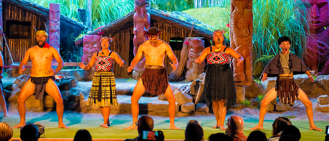 Māori performers in traditional dress on stage, performing a powerful haka for an audience in Rotorua.